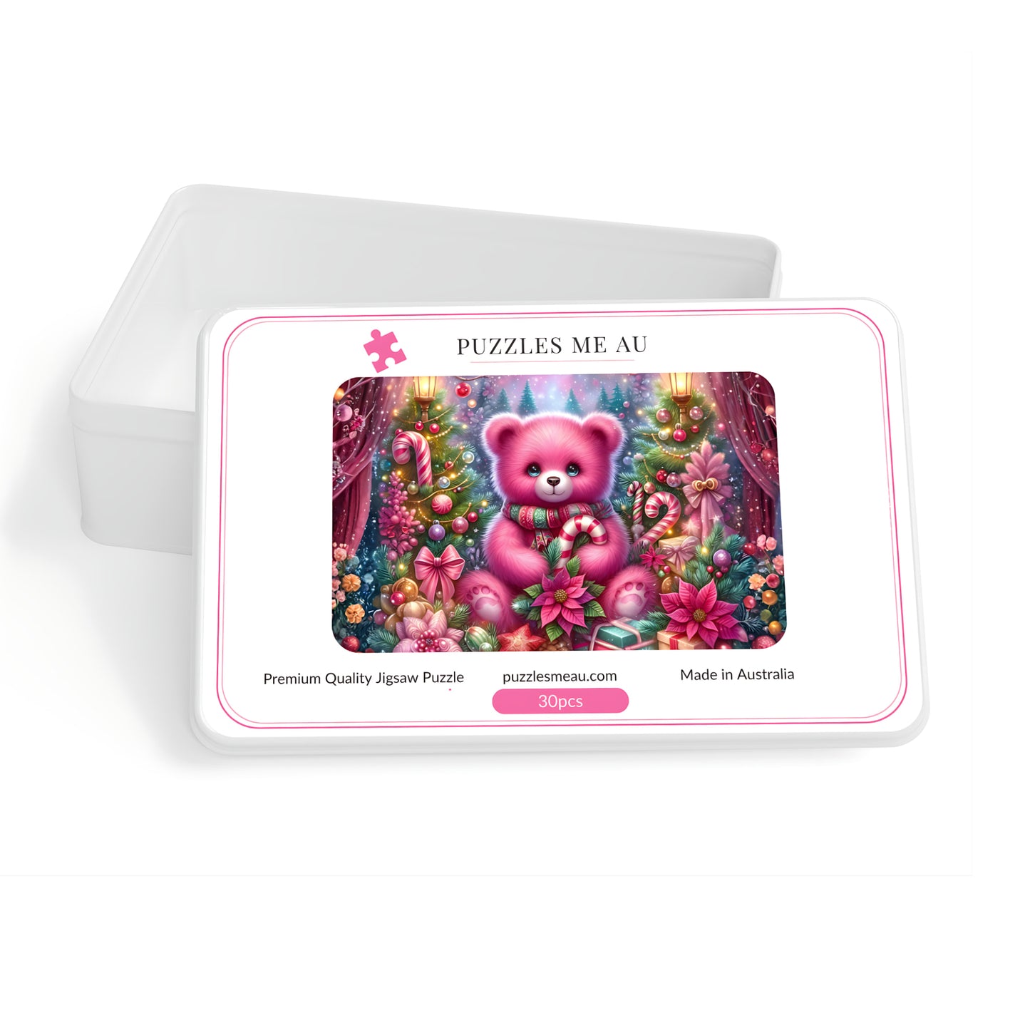A jigsaw puzzle box with a white lid leaning behind it on a white background. The front of the box shows a colorful illustration of a pink teddy bear in a decorated Christmas tree scene, with the text 'PUZZLES ME AU' and 'puzzlesmeau.