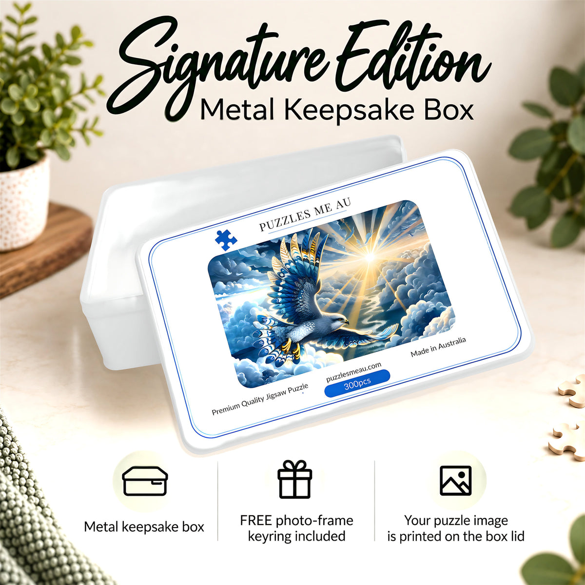 A white metal keepsake box shown on a light beige surface with decorative plants and small objects around it. The lid features a printed puzzle cover design with a blue falcon bird, clouds, and bright sun rays.